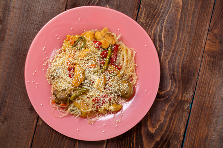 Funchoza with chicken and vegetables in teriyaki sauce garnished with sesame seeds in a plate on a wooden table.copy space Horizontal photoの写真素材