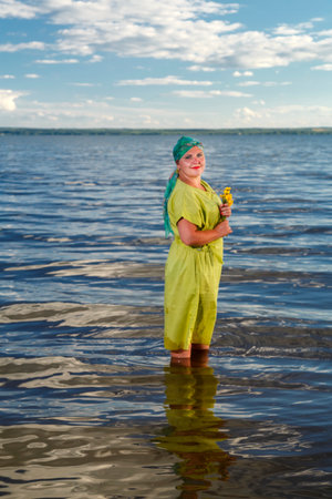 A Jewish woman in a green dress and a scarf with water lilies in her hands in the water of a lake on a sunny day. vertical photoの写真素材