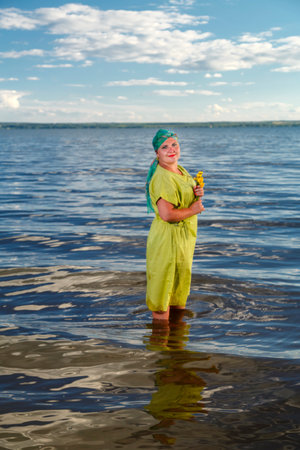 A Jewish woman in a green dress and a scarf with water lilies in her hands in the water of a lake on a sunny day. vertical photo.の写真素材