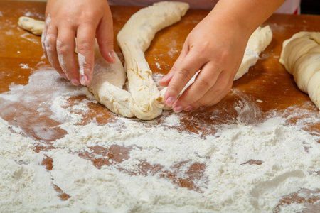 The hands of a Jewish woman weave challah with a pigtail for Shabbat on a wooden table in flour. horizontal photoの写真素材
