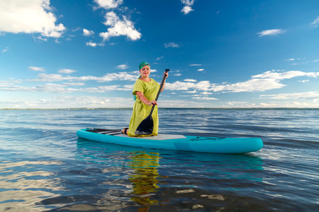 a woman in a dress and a scarf on a sapboard floats on her knees on the lake. horizontal photoの写真素材