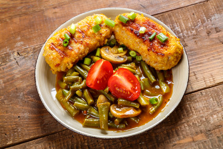 Cutlets with green beans and mushrooms in tomato sauce in a plate garnished with cherry tomatoes and green onions. horizontal photoの写真素材