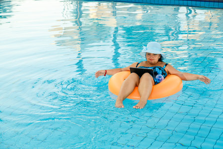 A woman in a sun hat in the pool in a swimming circle with a laptop communicates via video link. Horizontal photoの写真素材