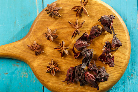 Hibiscus flowers and star anise on a wooden board on a blue table. horizontal photoの写真素材