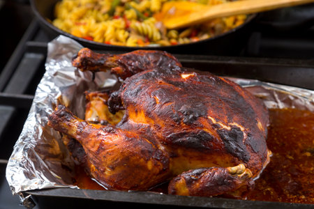 Whole chicken baked in sauce on foil in the background a frying pan with pasta. horizontal photoの写真素材