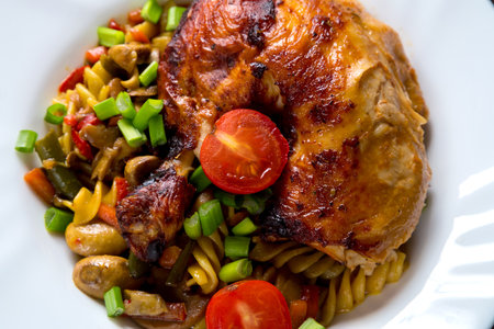 Pasta with vegetables in sauce and baked chicken leg with tomatoes sprinkled with green onions on a...