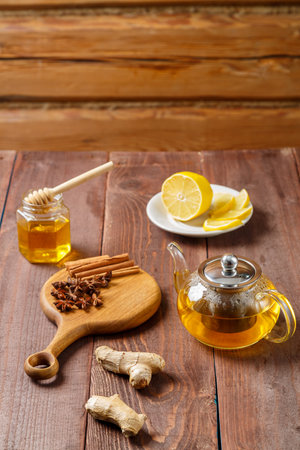 lemongrass tea teapot next to anise, ginger and cinnamon sticks on a round wooden board and honey and lemon. vertical photoの写真素材