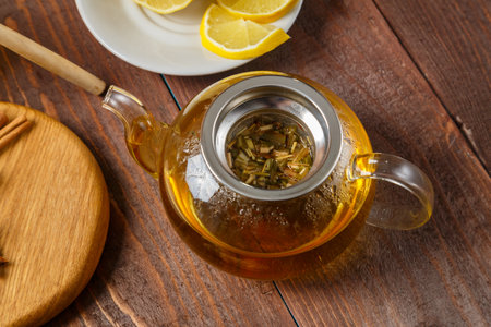 Transparent teapot of lemongrass tea next to anise, ginger and cinnamon on a round wooden board. horizontal photoの写真素材