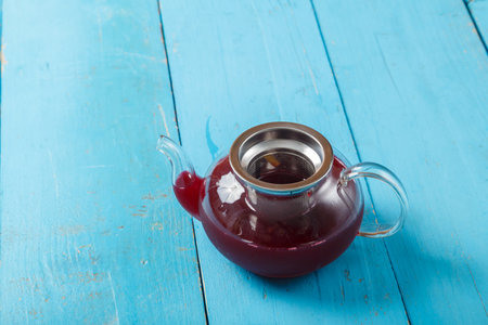 Teapot with hibiscus tea and transparent cherry on a blue wooden table. horizontal photoの写真素材
