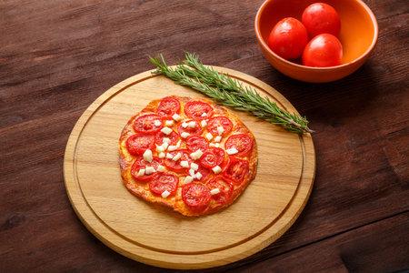 Homemade pizza with tomatoes and mozzarella on a round wooden board next to a sprig of rosemary and tomatoes. horizontal photoの写真素材