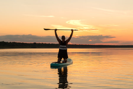 A man on a SUP board with a paddle above his head at sunset against the background of a golden sky...