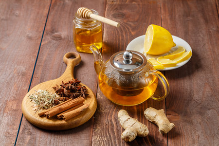 A transparent mug of lemongrass tea on a table next to anise, cinnamon, ginger and honey on a wooden board. horizontal photoの写真素材