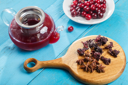 Kettle of hibiscus tea with cherries next to the table on a wooden board anise and cinnamon and hibiscus flowers and cherries in a plate. horizontal photoの写真素材