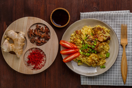 Thai chicken rice garnished with green onions on a wooden table next to a soy sauce napkin and a wooden fork next to anise saffron and ginger. horizontal photoの写真素材