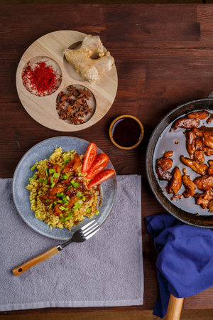 Fried chicken pieces in soy and pad thai sauce in a pan on a blue napkin on a table with a plate and spices. vertical photoの写真素材