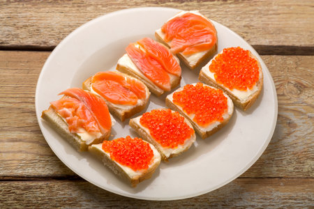 Toasts with red caviar and trout and butter on a plate on a wooden table. horizontal photoの写真素材