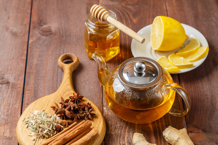 A transparent mug of lemongrass tea on a table next to anise, cinnamon, ginger and honey and a teapot with tea on a wooden board. horizontal photoの写真素材