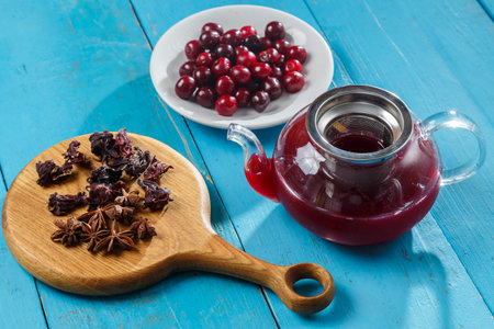 Kettle of hibiscus tea with cherries next to the table on a wooden board anise and cinnamon and hibiscus flowers and cherries in a plate. horizontal photoの写真素材