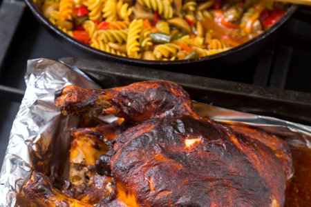 Whole chicken baked in sauce on foil in the background a frying pan with pasta. horizontal photoの写真素材