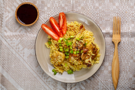 Chicken rice in teriyaki sauce garnished with green onions on a wooden table next to soy sauce on a gray tablecloth next to a wooden fork. horizontal photoの写真素材