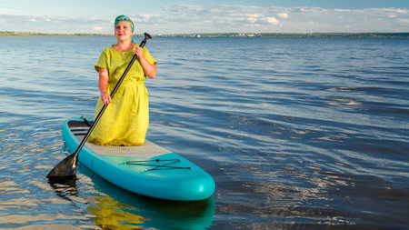 A Jewish woman in a Kisui Rosh headdress on a kneeling SUP board floats on the lake. horizontal photoの写真素材