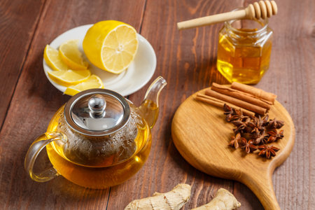 lemongrass tea teapot next to star anise, and cinnamon sticks on a round wooden board and honey and lemon. horizontal photoの写真素材