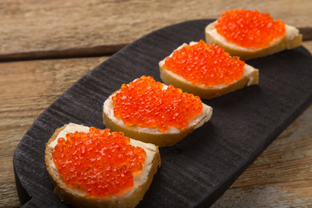 Toasts with red caviar and butter on a black serving board on a wooden table. horizontal photoの写真素材