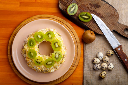 Layered salad with chicken and kiwi nuts next to quail eggs on a kiwi napkin on a board and a knife. horizontal photoの写真素材