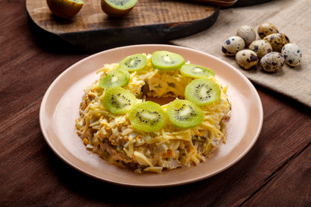 Layered salad with chicken and kiwi next to the board kiwi and quail eggs on the table horizontal photoの写真素材