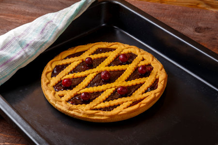 Shortcrust pastry cherry pie decorated with cherries and pastry grill on a baking sheet next to a white towel. horizontal photoの写真素材
