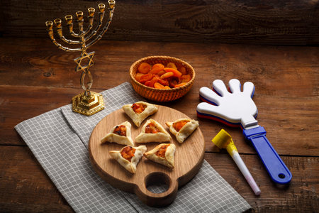 cookies triangles gometashi mishloach manot for Purim laid out on a wooden board on a napkin next to the menorah rattles and whistle. horizontal photoの写真素材