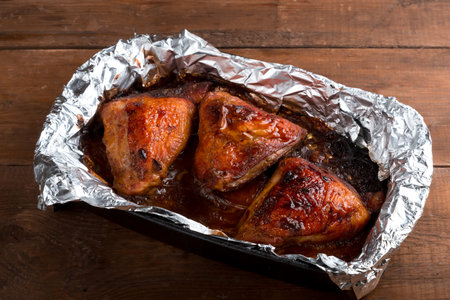 Baked chicken thigh in spices and crispy sauce on foil on a wooden table. horizontal photoの写真素材