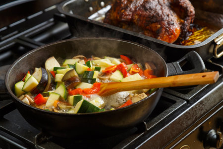 A frying pan with stewed vegetables on a plate next to a tray with baked chicken. horizontal photoの写真素材