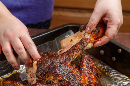 Women's hands tear off a ham from a whole baked chicken in a baking sheet. horizontal photo.の写真素材