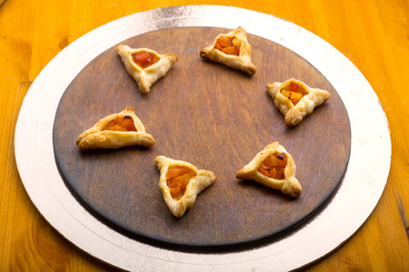Triangular gomentashi cookies for the holiday of Purim on a blackboard are laid out on a round board on a light table. horizontal photo.の写真素材