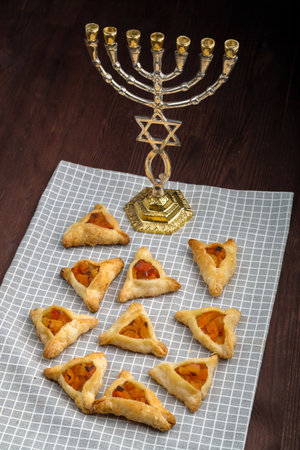 Homemade gomentashi cookies for the Jewish holiday of Purim on a checkered napkin next to the menorah. vertical photoの写真素材