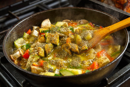 A frying pan with stewed vegetables and a wooden spoon on the stove . horizontal photoの写真素材