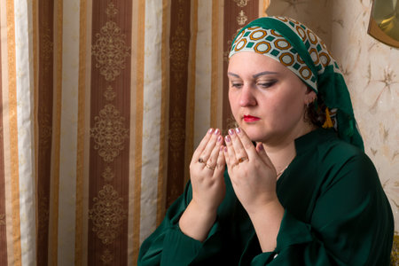 A woman in a green dress and headscarf reads a prayer. horizontal photoの写真素材