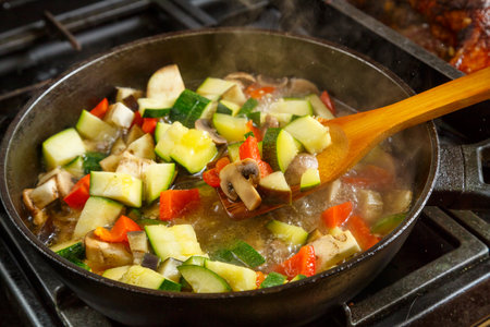 Frying pan with stewed vegetables in sauce and spices and a wooden spoon on the stove . horizontal photo.の写真素材