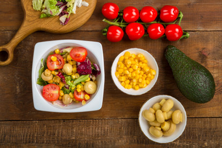 salad with lettuce and cherry tomato with avocado olive oil in a white plate on a wooden table next to all the ingredients. horizontal photoの写真素材