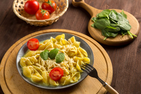 Pasta in cream sauce with cheese garnished with spinach with a fork on a round wooden stand. horizontal photo.の写真素材