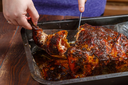 Women's hands tear off a leg from a whole baked chicken in spices in a baking sheet. horizontal photo.の写真素材