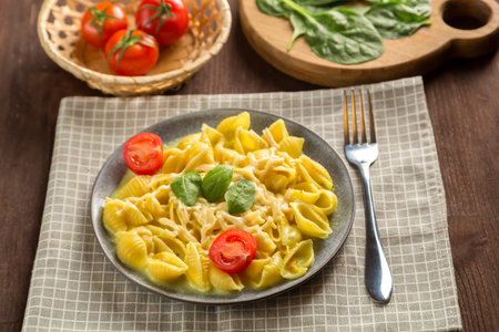 Pasta in a creamy sauce with cheese with a fork next to tomatoes, a knife and greens on a linen napkin. horizontal photo.の写真素材