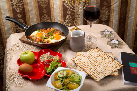 A set table for the Passover Seder with traditional matzah, wine, maror and shakshuka in a frying...