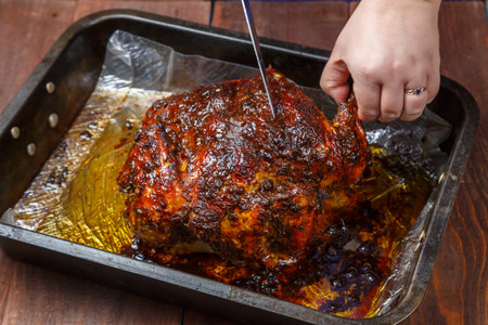 Women's hands tear off a leg from a whole baked chicken in a baking sheet with a knife. horizontal photo.の写真素材