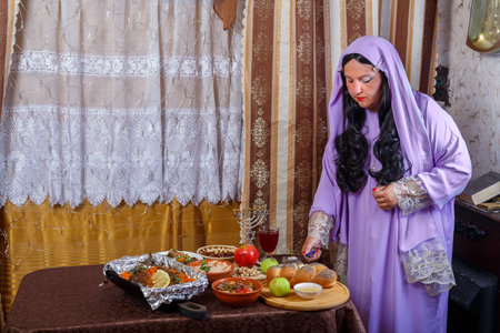 A Jewish woman in a wig and a veil falling from her hair and a long dress lights candles on Rosh Hashanah, Shabbat at the set table. horizontal photoの写真素材