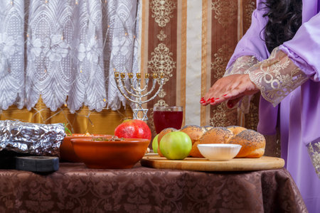 A Jewish woman reads a blessing on candles at a set table on the Jewish holiday of Rosh Hashanah before a meal. Horizontal photo.の写真素材