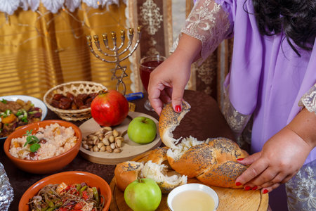 A woman's hand breaks the challah at the set table on the Jewish holiday Rosh Hashanah before the meal. Horizontal photo.の写真素材