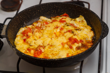 Scrambled eggs with tomatoes and sprinkled with cheese in a frying pan on the stove. horizontal photoの写真素材