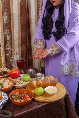 A Jewish woman in a wig and a veil falling from her hair and a long silk dress reads a blessing on the candles on Rosh Hashanah, at the set table. Vertical photoの写真素材